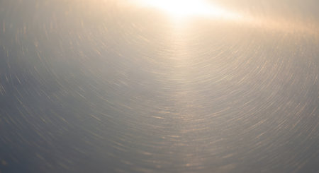 A high-quality texture shot of a brushed silver metal surface features circular scratch patterns and a bright light reflection. The abstract and industrial background conveys concepts of durability, modern design, and clean materials.の素材