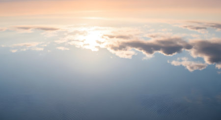 A mesmerizing reflection of a pastel-colored sunset sky on a calm water surface. The soft blues, pinks, and oranges of the clouds are mirrored perfectly with gentle ripples disturbing the texture. This abstract nature background evokes feelings of serenity, tranquility, and dreamlike beauty.の素材
