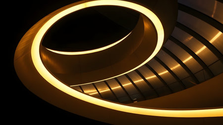 A low-angle abstract view of a modern architectural spiral structure illuminated by warm golden lights against a dark background. The sweeping curves and geometric lines create a futuristic and artistic composition.の素材