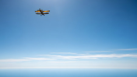 A small yellow vintage biplane flying high in a vast, clear blue sky. The minimalist composition captures the freedom of flight, with ample copy space in the lower portion of the frame where the sky fades into a lighter hue.の素材