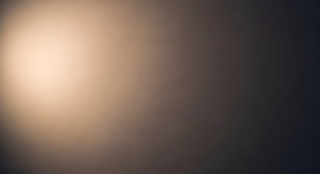 A textured abstract background displaying a gradient from warm light to deep shadow. The minimalist wall surface offers ample copy space and a moody, atmospheric aesthetic suitable for design overlays.の素材