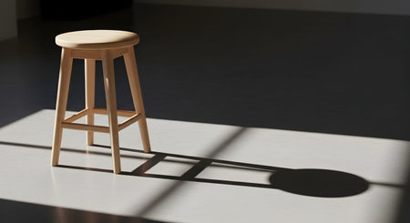 A simple wooden stool stands alone in an empty room, illuminated by strong directional light that casts a distinct, long shadow on the floor. The minimalist composition focuses on form, light, and solitude.の素材