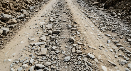 A perspective view of a rough, rocky dirt road covered in loose stones and tire tracks. The rugged terrain suggests a remote location, off-road travel, or a construction haul road.の素材