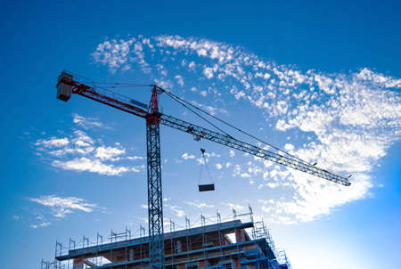 CAGLIARI, SARDINIA, ITALY - 07/23/2020: 85/5000 a tower crane with hoists builds a future modern condominium building, background with blue sky with cloudsのeditorial素材