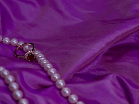 Golden gem Ruby Ring with pink pearl necklace on pink surface silk backgroundの写真素材