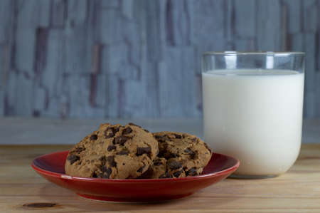 Chocolate Chip Cookies on red plate and Milk on wooden table - copy space area