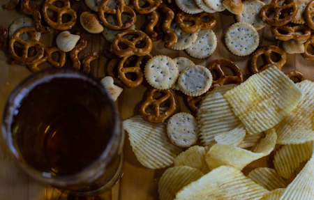 Cold beer and wavy potato chips in a bowl and salty snacks pretzel on a wood table close up from aboveの写真素材