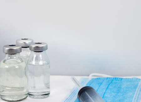 Coronavirus COVID-19 Vaccine Vial, Syringe and blue Medical Face Mask on white background - close up copy space areaの写真素材