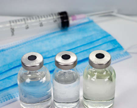 Coronavirus COVID-19 Vaccine Vial, Syringe and blue Medical Face Mask on white background - close up...