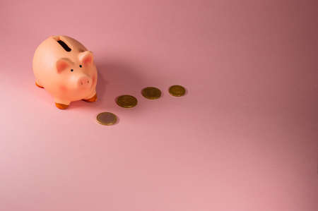 Close-Up Of pink Piggy Bank With some Coins Against Pink Background - Concept of saving money - Copy space areaの写真素材