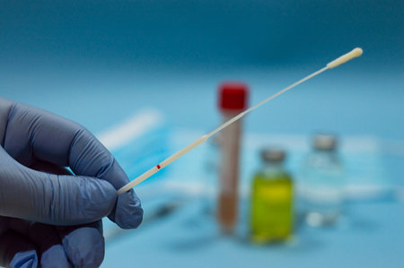 Doctor's hand with swab for coronavirus test with blurred background with vaccines and medical mask on blue background, empty copy space areの写真素材
