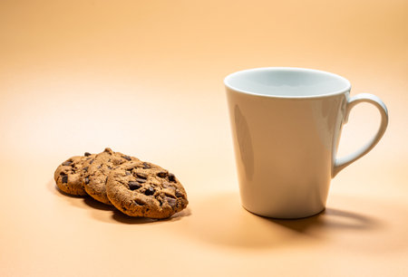 Close up white mug of milk and three dark chocolate chip cookies on empty background, copy space area. Yellow golden backgroundの写真素材