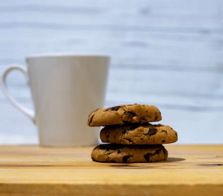 Pile of threeChocolate chips cookies with a coffee cup on a wooden tableの写真素材
