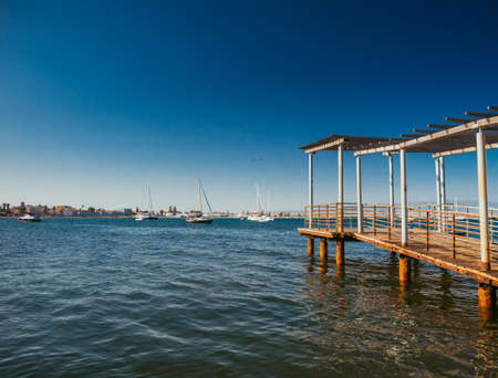 long wooden quay on the sea towards the horizon with moored sailboatsの写真素材