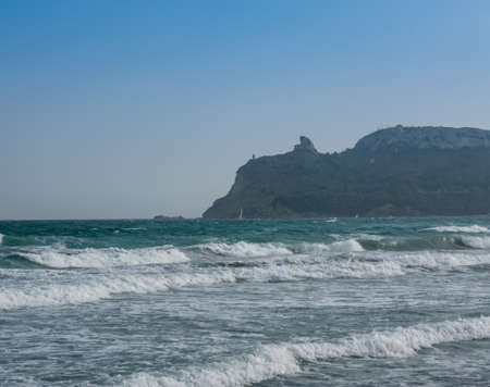 view from the rough mediterranean sea with waves with foam of the Sella del Diavolo mountain in Sardinia Italy, cloudless skyの写真素材