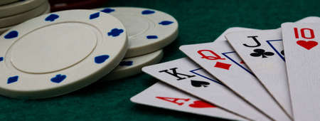 Royal straight flush poker cards with stack of poker chips on a green felt table background, web...