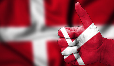 hand with thumbs up in approval with the Danish flag painted. Image with flag background area out of focus, copy space areaの写真素材