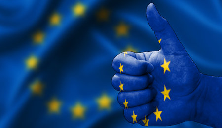 hand with thumbs up in approval with the European Union flag painted. Image with flag background area out of focus, copy space areaの写真素材