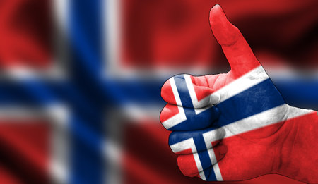 hand with thumbs up in approval with the Norwegian flag painted. Image with flag background area out of focus, copy space areaの写真素材