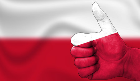 hand with thumbs up in approval with the polish flag painted. Image with flag background area out of focus, copy space areaの写真素材