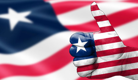 hand with thumbs up in approval with the Liberian flag painted. Image with flag background area out of focus, copy space areaの写真素材