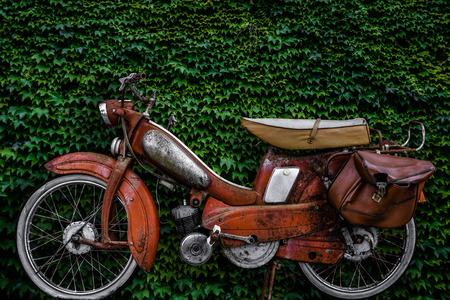 Vintage 60s French Moped Or Scooter With Pannier Bag And Flat Tyre Or Scooter Against An Ivy Backgroundの写真素材