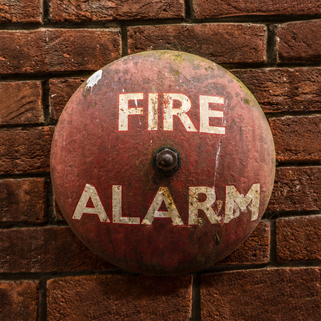 Rustic Vintage Fire Alarm Bell Against A Red Brick Wallの写真素材