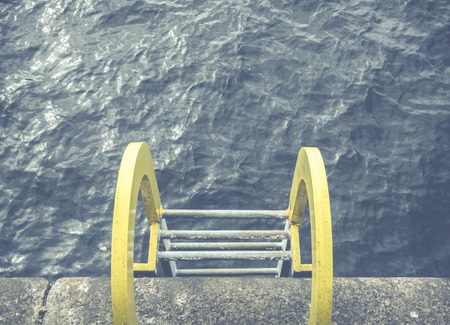 Conceptual Image Of A Yellow Ladder Into Blue Ocean Water At A Harborの写真素材