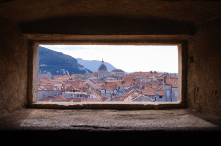 View Of Dubrovnik Old Town Rooftops And Church Dome Framed Through A Battlement Window In The Historic City Walls, Croatiaの写真素材