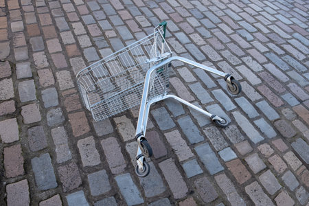 An Abandoned Shopping Trolley (Cart) Lying On Its SIde On A Cobblestone Streetの写真素材