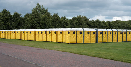 Long Row Of Yellow Portable Chemical Toilets Set Up For A Music Festival Under A Cloudy Skyの写真素材