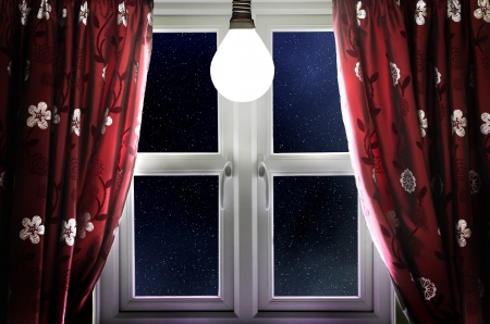 Light bulb shining in window with curtainsの写真素材