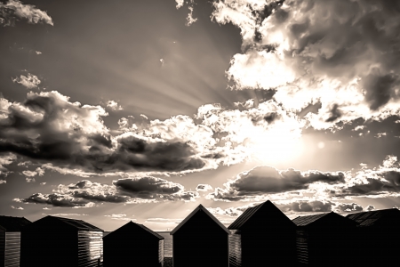 Beach huts in black and white with sun setting through cloudsの写真素材