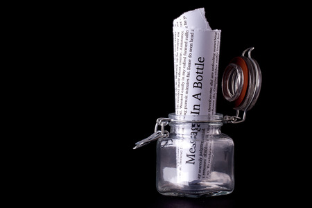 Message in a bottle paper note inside a glass jar with a black wall の写真素材