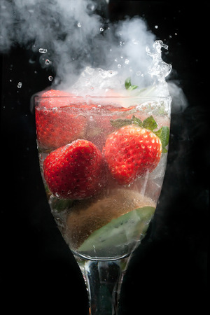 Cocktail of fruit in a glass exploding with steam and smoke, with water movement frozen, all on a black backgroundの写真素材