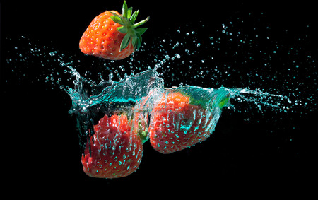 Strawberries dropped into water with splashes on a black backgroundの写真素材