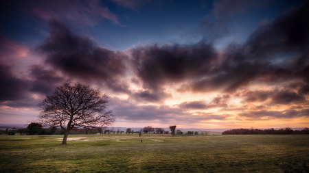Golf course landscape with a red sunset sky with dark cloudsの写真素材