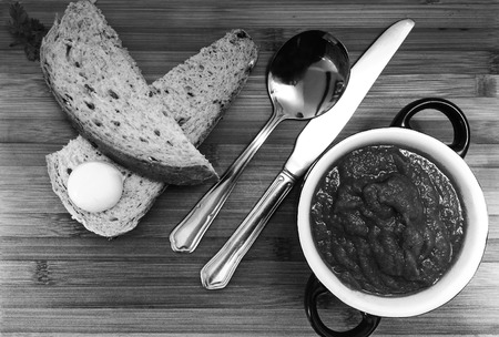 Homemade traditional fresh soup and bread on a wooden board viewed from above in black and whiteの写真素材