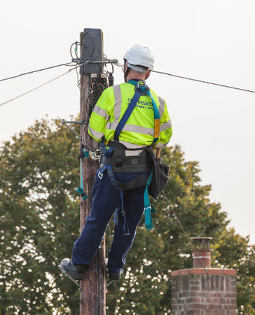 FAKENHAM, NORFOLK / UK - 10th OCTOBER 2016: Openreach BT engineer fixing cables up a pole. UK internet and telephone infrastructure provider at work providing internet and telephone services to rural locationsのeditorial素材