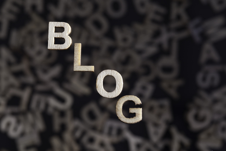Blog wooden letters text on an angle created in wood floating above random letters below out of focus on a black backgroundの写真素材