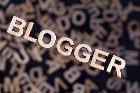 Blogger wooden letters text created in wood floating above random letters below out of focus on a black backgroundの写真素材