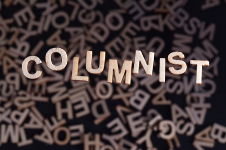 Columnist wooden letters created in wood floating above random letters below out of focus on a black backgroundの写真素材