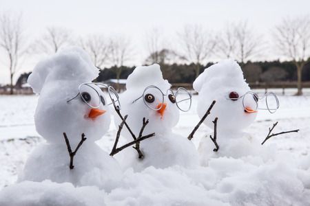 Three cute snowman characters with reading glasses and snow mohican hair cuts. Snow fallen all around at winter timeの写真素材