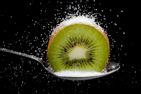 Kiwi fruit cut in half on a spoon with sugar granules pouring over the fruit showing conectp of hidden sugars in fruit. black backgroundの写真素材