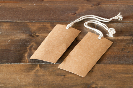 Two blank brown labels with string tags. Empty tags to be used for text or writing signs. Laid on a wooden rustic floor. Concept for sales, finance and business.の写真素材