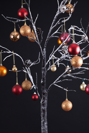 Modern Christmas tree with bare snow covered branches, decorated with hanging glitter balls, all on a black backgroundの写真素材