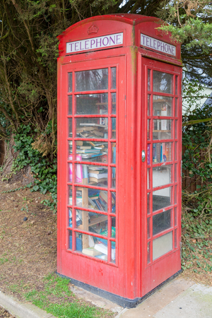 Red public telephone box in the UK. Phone booth full of books acting as a local mini library. Red phone boxes are very iconic in England and have been around since about 1924. Although these landmarks are still around, not all of them are working telephone boxes any more, this one was converted into a mini local libraryの写真素材
