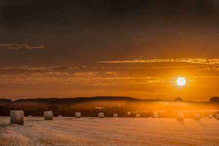 Hay bales at sunset with skies clearing to show stars at night. Beautiful panoramic evening orange sun over rural crop fields in Norfolkの写真素材