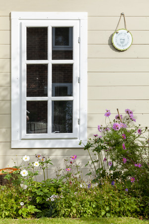 Summer flowers against a wooden summhouse building window in the gardenの写真素材