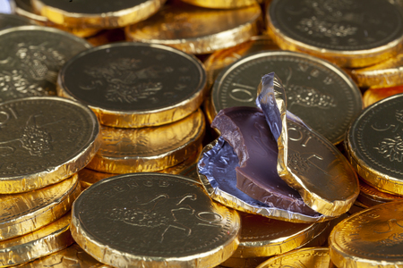 Chocolate money pile of gold coins. Edible sweets covered in foil as pretend money. One open coin half eatenの写真素材